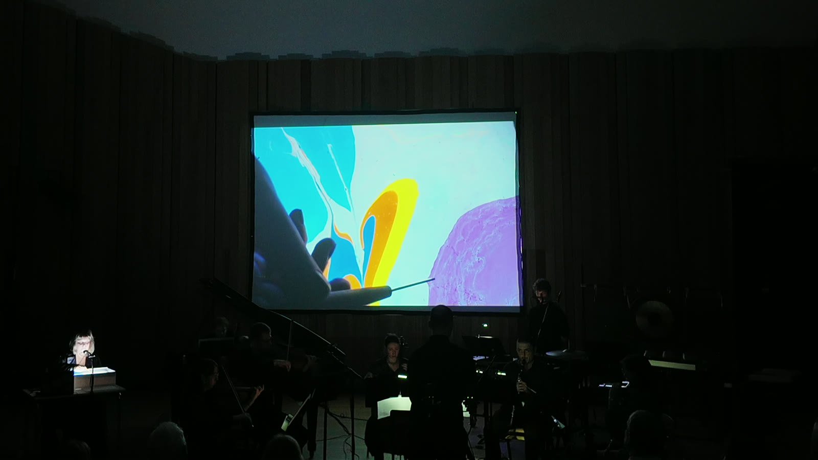 a stylus draws through the colour field while the ensemble plays beneath the projection